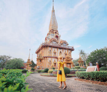 Woman in yellow dress walking toward ornate golden temple at Wat Chalong in Phuket.