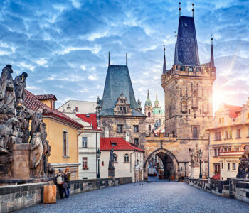 Charles Bridge at sunrise with statues and gothic towers leading into Prague’s Old Town.