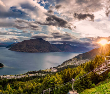Panoramic view of Queenstown, New Zealand, with Lake Wakatipu and surrounding mountains at sunset.