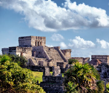 Ancient Mayan ruins of Tulum perched on a cliffside above lush greenery and blue skies.