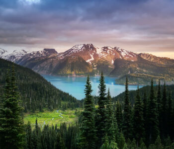 Snow-dusted mountains encircle a turquoise lake near Whistler, with evergreen trees filling the foreground.