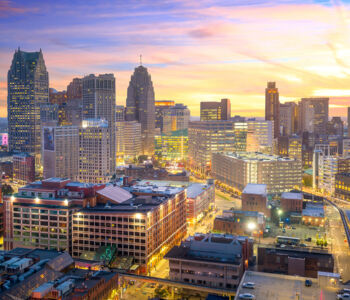 Detroit skyline at sunset with glowing city lights and pastel skies over downtown.