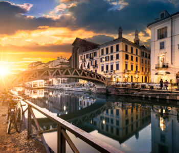 Sunset along Milan’s Navigli canal district with historic buildings, reflections on the water, and bicycles lining the walkway.