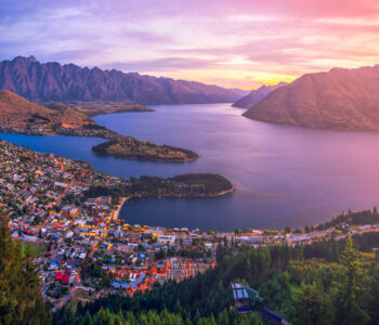 Paragliders soaring above Queenstown with Lake Wakatipu and snow-capped peaks in the background.