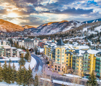 Sunset over Vail Village with colorful alpine buildings, snowy slopes, and mountain ranges in the background.