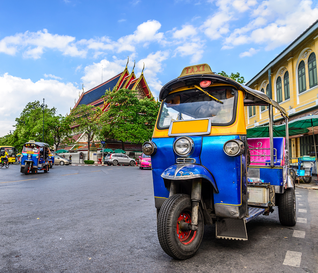 Colorful tuk tuk parked in front of Wat Pho temple in Bangkok, Thailand with blue skies and bustling street scene