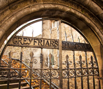 Iron gate marking the entrance to Greyfriars Kirkyard in Edinburgh, framed by old stone walls and autumn leaves.