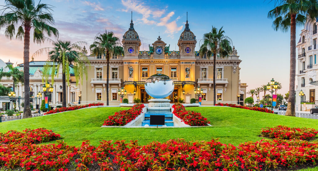 Grand facade of the Monte-Carlo Casino framed by palms and gardens, twilight sky above Place du Casino in Monaco