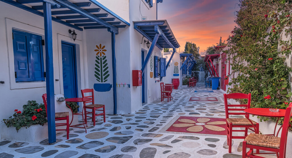Traditional Greek houses in Ano Mera village, Mykonos, with vibrant flowers and painted walkways.
