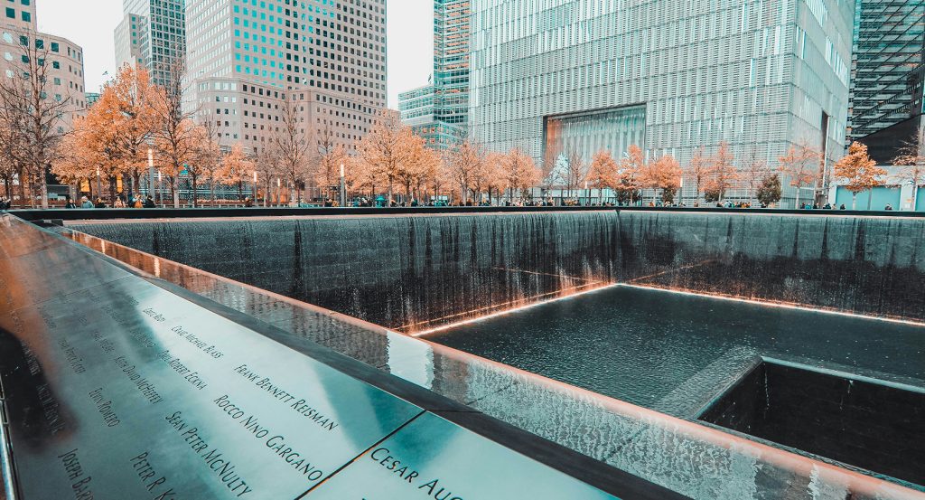 Close-up of bronze name panels at the 9/11 Memorial during the day with waterfalls in the background.