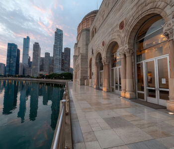 Exterior of Chicago’s historic Adler Planetarium at sunrise with the city skyline reflected in the calm waters of Lake Michigan.