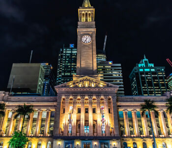 Brisbane City Hall illuminated at night with clock tower against modern skyline