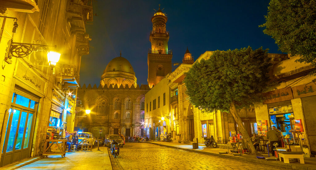 Lantern-lit view of Al-Muizz Street with mosques and shops