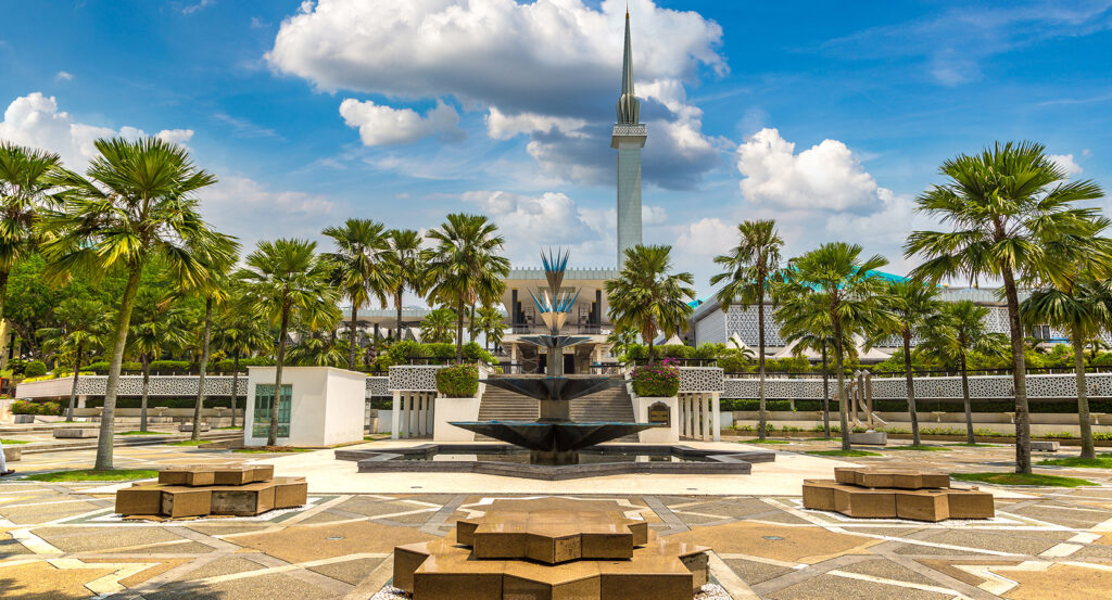 Masjid Negara in Kuala Lumpur with modern Islamic architecture, star-shaped fountain, and lush palm gardens.