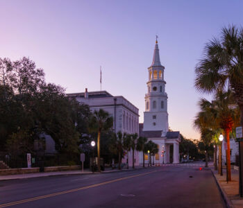 St. Philip’s Church in Charleston at sunrise with soft pastel light and palm trees lining the street.