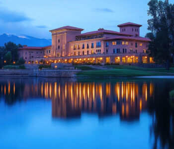 The Broadmoor resort illuminated at blue hour with warm lights reflecting on a still lake.