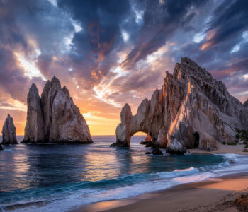 Dramatic sunset over El Arco rock formations in Cabo San Lucas with waves crashing along the shoreline.