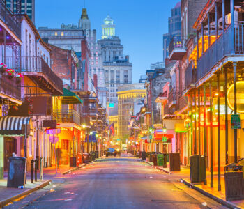 Bourbon Street in the French Quarter at dusk with glowing neon signs and historic iron-balcony buildings.