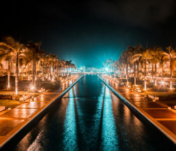 Nighttime view of illuminated palm-lined promenade and reflecting pool at Punta Cana resort.