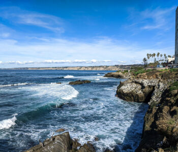 Waves crashing against the rocky cliffs of La Jolla Cove under a bright blue sky in San Diego.