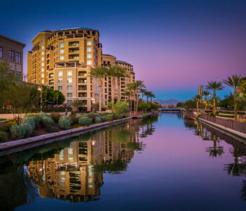 Scottsdale waterfront at sunset with luxury residences, palm trees, canal reflections, and upscale desert architecture.