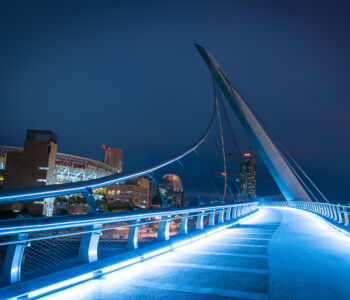 Night view of the Harbor Drive Pedestrian Bridge leading toward Petco Park in San Diego, illuminated against the city skyline.