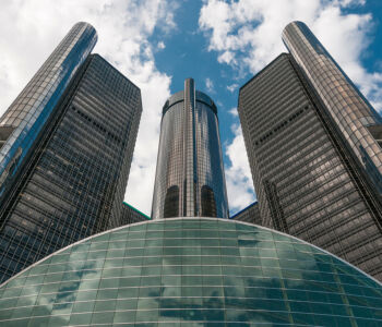 Upward view of the Renaissance Center towers and curved glass dome against a bright sky.