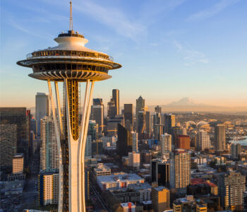 Seattle skyline at sunset with the Space Needle rising above downtown and Mount Rainier visible in the distance.