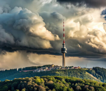 Dramatic storm clouds forming over a mountaintop communications tower surrounded by dense green forest.