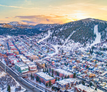 Aerial sunset view of Park City, Utah, with snow-dusted rooftops and mountain ski runs behind the town.