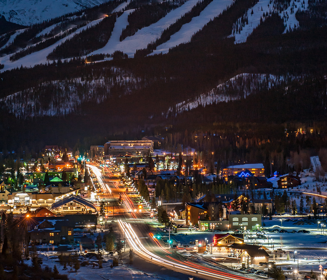 Downtown Winter Park, Colorado illuminated at night with ski slopes glowing in the distance
